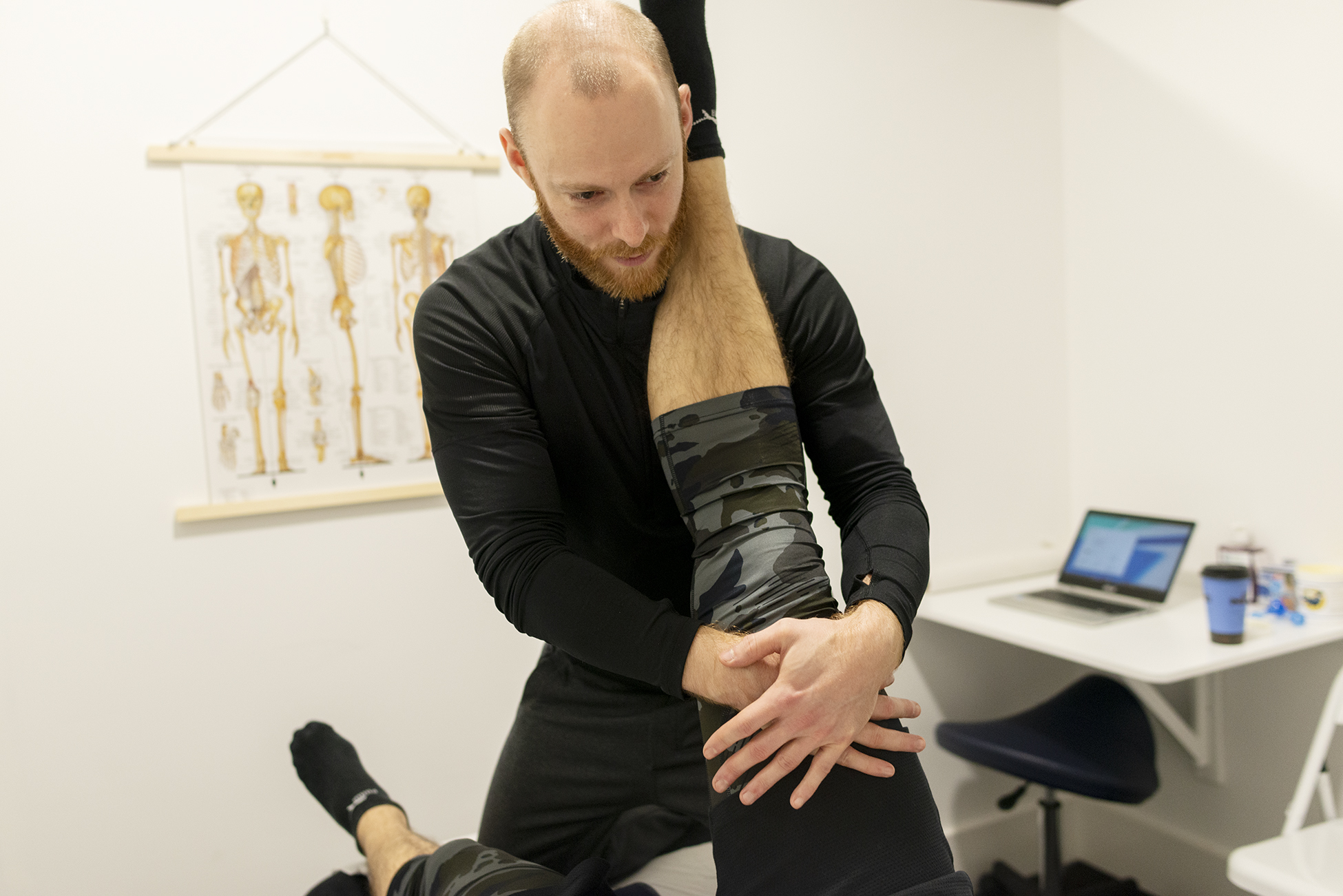 A sports therapist stretches his client's hamstrings